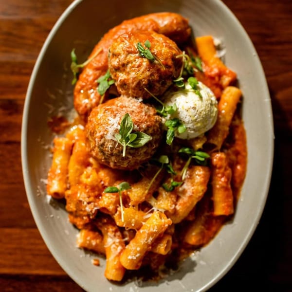 Rigatoni pasta with meatballs, sausage, ricotta, and fresh herbs in a red sauce.