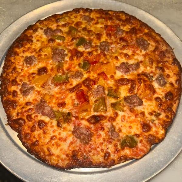 A whole, cooked pizza with melted cheese, sausage, and colorful bell peppers on a metal pan.