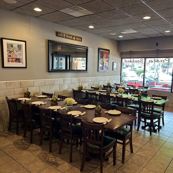 An empty restaurant dining room with dark wooden tables, chairs, and tiled floors.
