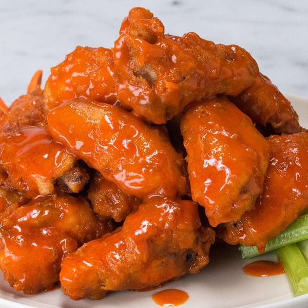 A close-up of a pile of bright orange buffalo chicken wings with celery sticks on a white plate.